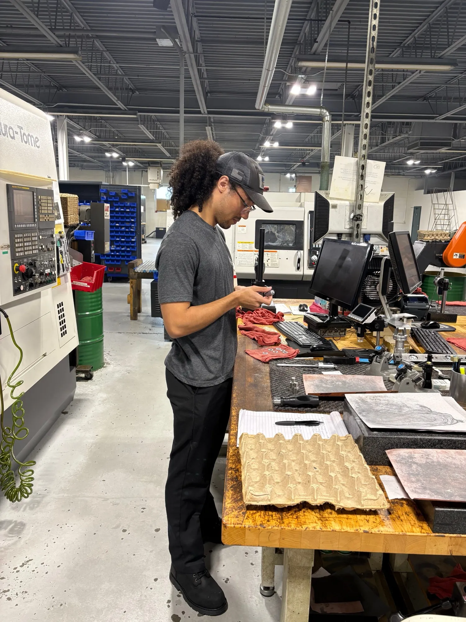 A CNC Manufacturing team member checking and handling machined parts at a bench beside the turning centers